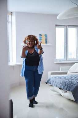 Vücut-pozitif kıvırcık kadın müzikten hoşlanıyor ve kameraya poz veriyor.
