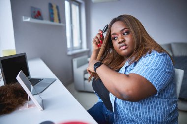 Ciddi bir kadın aynanın önünde saçını tarıyor.