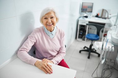 Neşeli yaşlı bayan dişçi masasında dinleniyor.