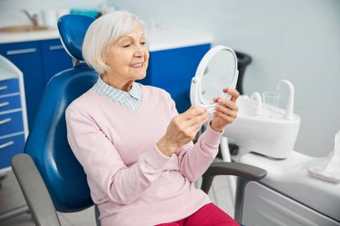 Yaşlı vatandaş masa aynasını karıştırıyor ve kendine bakıyor.