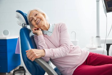 Dişçi koltuğunda uzanmış, kulağına dokunan hayat dolu bir kadın.