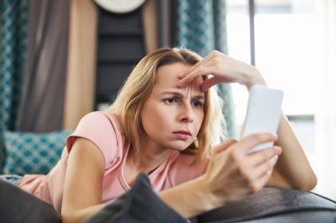 Kafası karışmış güzel bir kadın cep telefonundan mesaj okuyor.