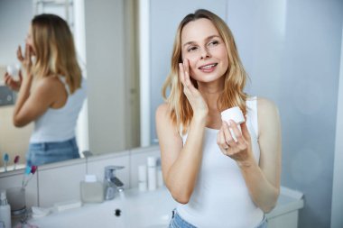 Güzel kadın banyoda yüz kremi kullanıyor.