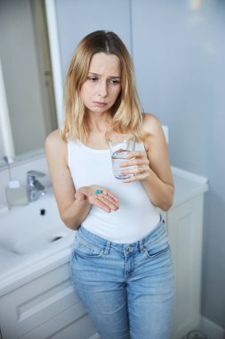 Evde hap alan üzgün genç bir kadın.