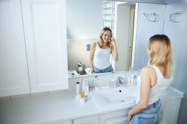 Cheerful young woman using eyelash curler in bathroom