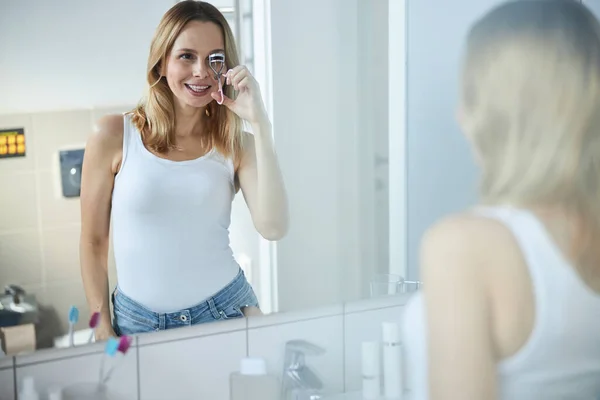 Charming young woman using eyelash curler in bathroom
