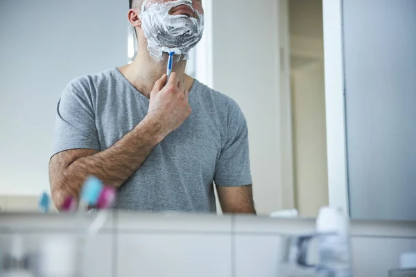 Young man shaving beard with razor in bathroom