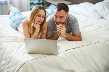 Sevgili çift dizüstü bilgisayar kullanıyor ve yatak odasında dinleniyor.