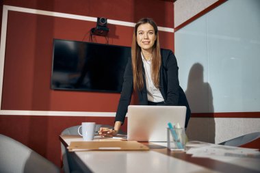 Kameraya poz veren takım elbiseli, memnun bayan çalışan.