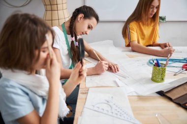 Dikiş atölyesinde güzel kızlar korse desenleri çiziyor.