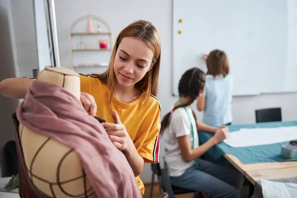 Charming girl working with mannequin in sewing workshop