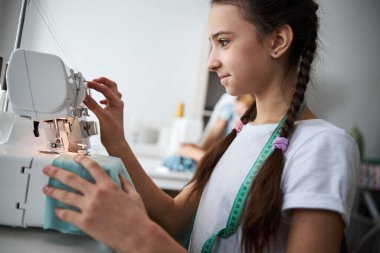 Atölyede modern dikiş makinesi kullanan sevimli bir kız.