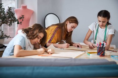 Çekici kızlar atölyede dikiş desenleri çiziyor.