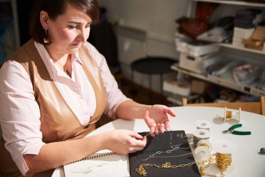 Zanaatkar kadın müşterisi için yeni bir zincir kolye yapıyor.