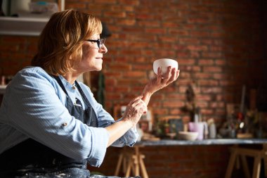 Elinde kilden kaseyle çömlek atölyesinde çalışan hoş bir yaşlı kadın.