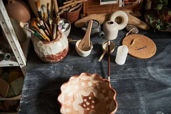 Tigela de barro e pincéis de tinta na mesa em oficina de cerâmica — Fotografia de Stock