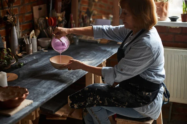 Nice female potter painting clay bowl in pottery workshop — Stock Photo, Image