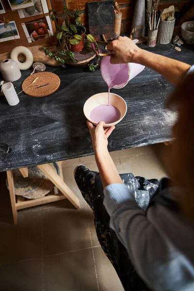 Жіночий гончар наливає рожеву фарбу на глиняну чашу в майстерню — стокове фото