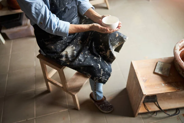 Γυναίκα αγγειοπλάστη με πήλινο μπολ κάθεται σε σκαμνί στο στούντιο κεραμικής — Φωτογραφία Αρχείου