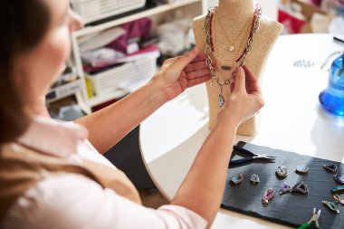Koyu renk saçlı kadın kuyumcu. El yapımı kolyelerini düzenliyor.