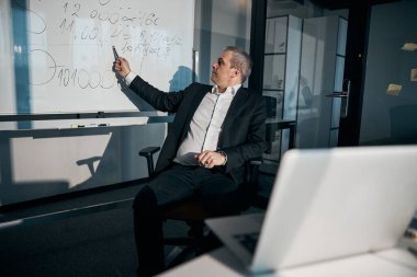 Erkek girişimci ofisteki beyaz tahtayı işaret ediyor.