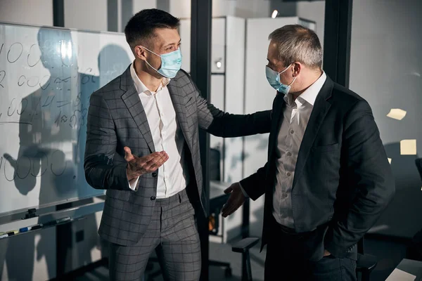 Business colleagues in medical masks communicating in office