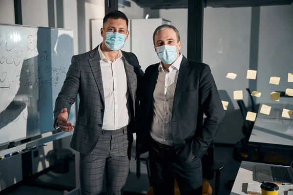 Бізнес-колеги в медичних масках, що стоять в офісі — стокове фото