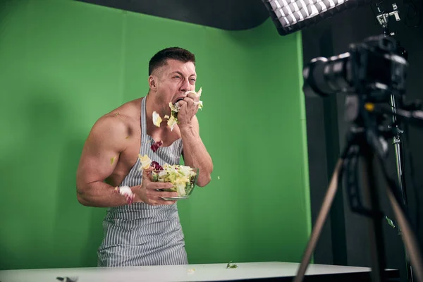 Atlético jovem gravação de vídeo e comer salada em estúdio — Fotografia de Stock