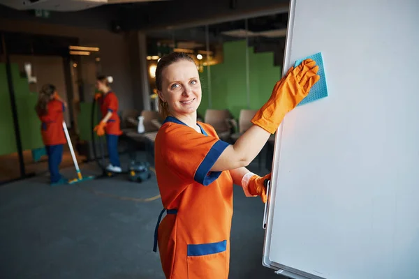 Pleased young woman in the uniform cleaning the conference room — Stock Photo, Image