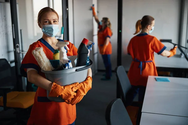Conserje femenina con productos de limpieza de pie entre sus colegas ocupados — Foto de Stock