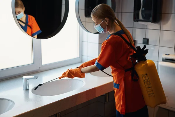 Limpiador en guantes de goma desinfectando el lavabo del baño — Foto de Stock