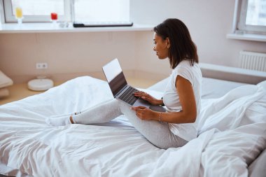 Yatak odasında dizüstü bilgisayar kullanan hoş bir genç kadın.