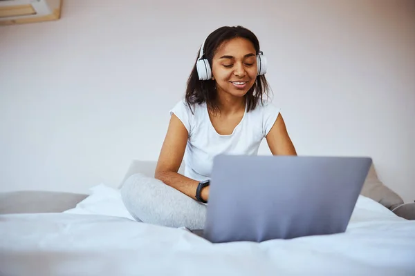 Giovane donna gioiosa in cuffia utilizzando il computer portatile a casa — Foto Stock