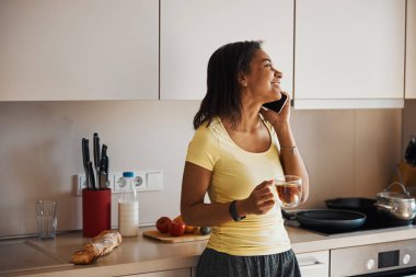 Mutfakta cep telefonuyla konuşan güzel genç bir kadın.