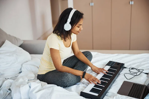 Γοητευτική νεαρή γυναίκα παίζει synthesizer και χρησιμοποιώντας φορητό υπολογιστή στο σπίτι — Φωτογραφία Αρχείου