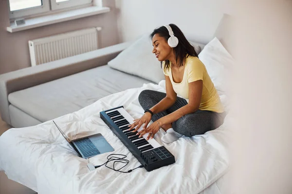 Affascinante giovane donna che gioca synth e utilizzando notebook a casa — Foto Stock