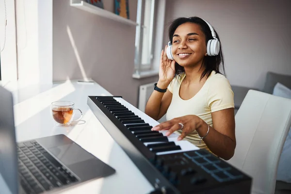 Χαρούμενη νεαρή γυναίκα παίζει synthesizer και τη χρήση σημειωματάριο στο σπίτι — Φωτογραφία Αρχείου