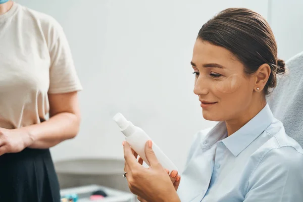 Woman examining a cosmetic product in the cosmetologist office — Stock Photo, Image