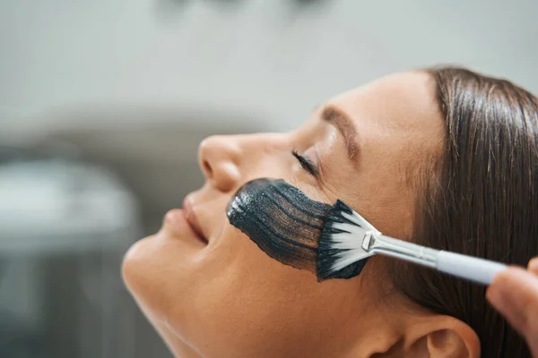 Рука дерматолога наносит средство для ухода за кожей на женскую щеку — стоковое фото