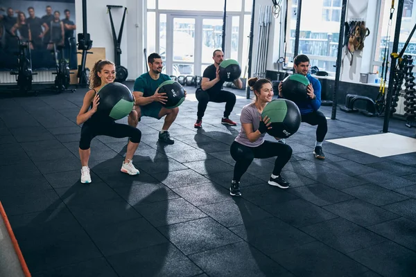 Spor salonunda çömelme hareketleri yapan genç sporcular. — Stok fotoğraf