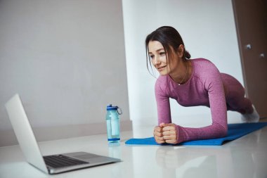 Sportif kadın kalas yapıyor ve evde dizüstü bilgisayar kullanıyor.