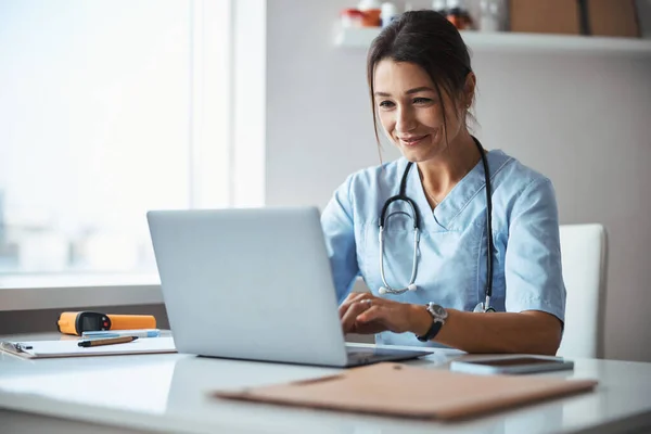 Joyeuse femme médecin à l'aide d'un ordinateur portable en clinique — Photo