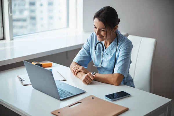 Alegre médico femenino usando un portátil moderno en el trabajo —  Fotos de Stock