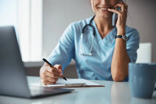 Joyeuse femme médecin parlant sur téléphone portable et écrivant sur presse-papiers — Photo