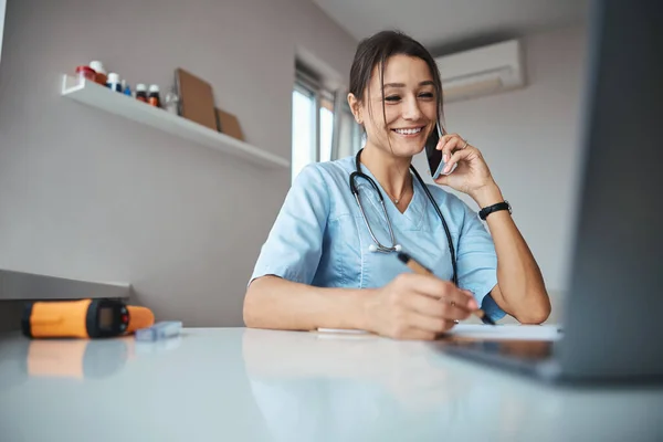 Alegre médico femenino teniendo conversación telefónica en el trabajo —  Fotos de Stock