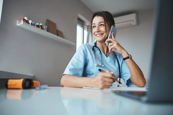 Encantadora doctora teniendo conversación telefónica en el trabajo —  Fotos de Stock