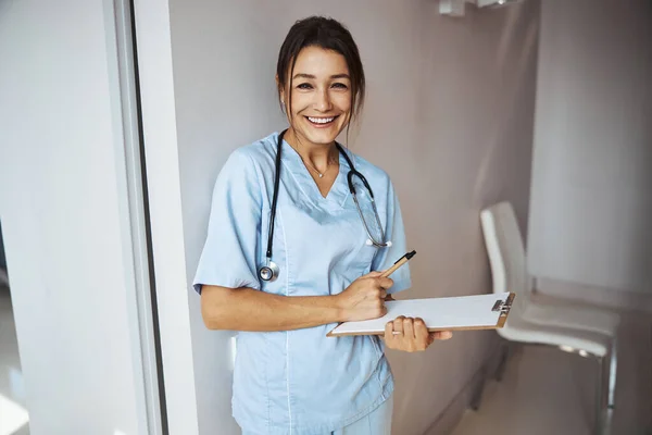 Joyeuse femme médecin avec presse-papiers debout dans la clinique — Photo