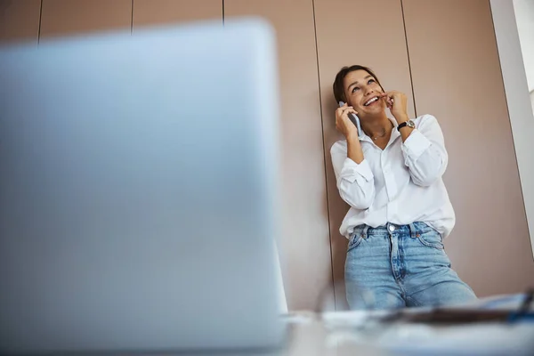 Glädjande ung kvinna pratar i mobiltelefon på jobbet — Stockfoto