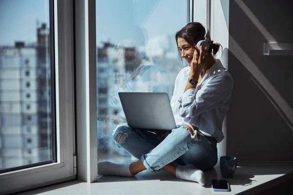 Femme gaie utilisant un ordinateur portable et écoutant de la musique à la maison — Photo