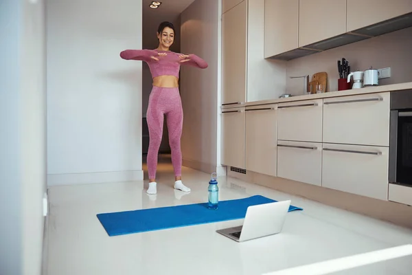 Mujer deportiva alegre usando el ordenador portátil y haciendo ejercicio en casa — Foto de Stock